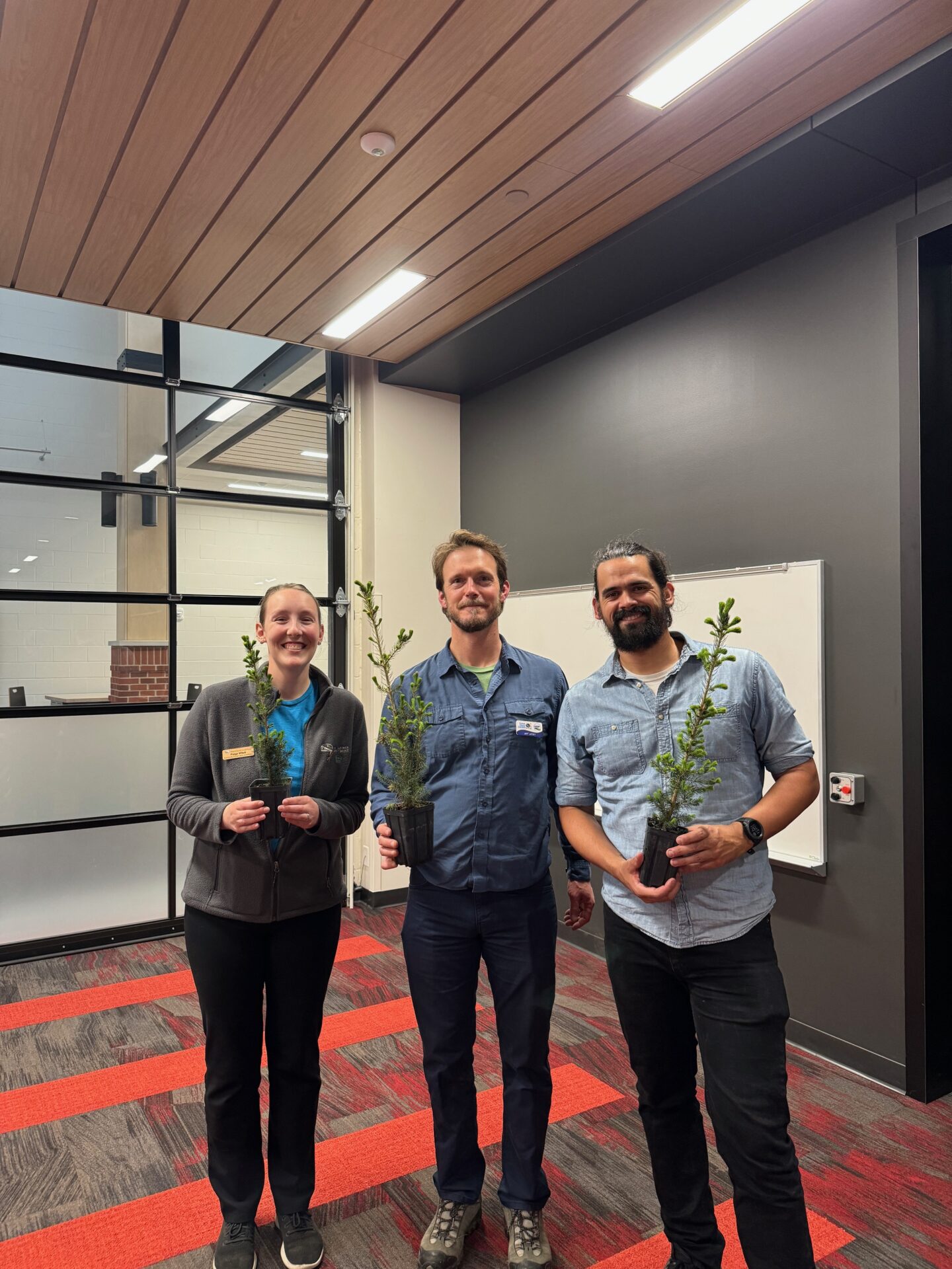 Flood resilience fellow Jackson Parr stands alongside Paige Witek of Door County Land Trust and Jeff Lutsey of the Door County Big Plant, all of whom hold tree saplings.