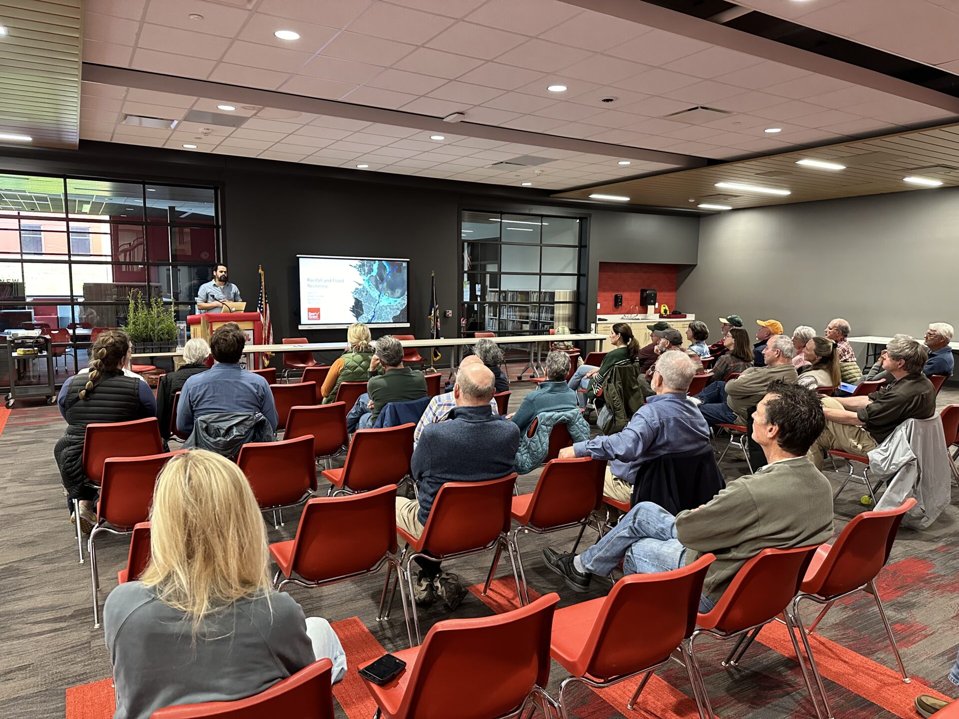 Jackson Parr delivers a talk at a podium in front of a room of people sitting in red chairs.