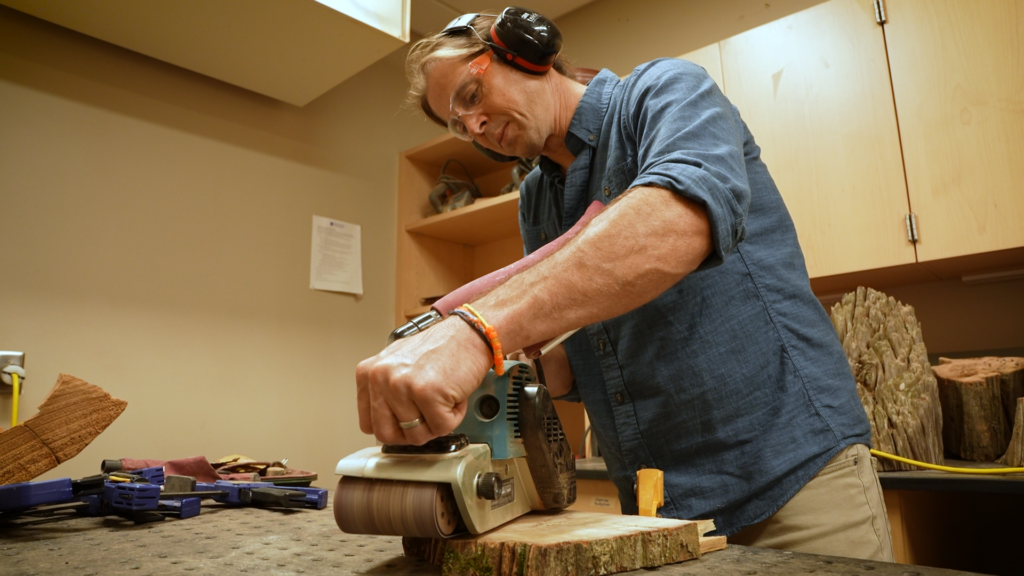 Evan Larson uses a belt sander in his workshop.