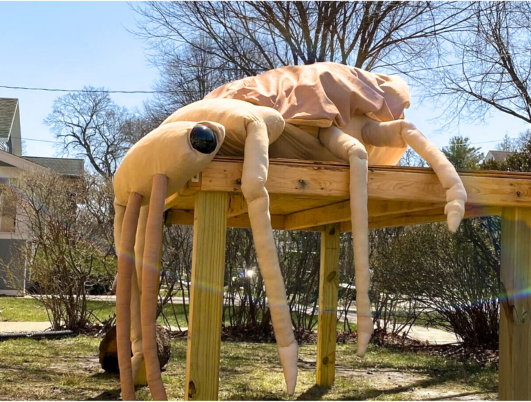 A giant, stuffed brown beetle sits on a wooden table outside