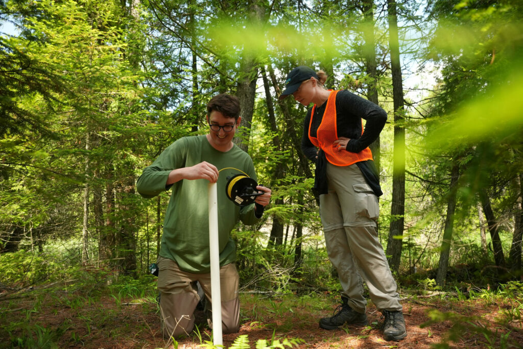 Graduate student Eric Kastelic and undergraduate researcher Lucie Carignan check in on a groundwater monitoring well that they installed at the Ridges Sanctuary, which gives them groundwater level measurements multiple times every hour.