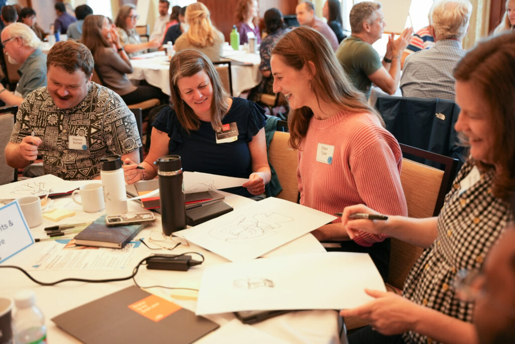 Participants at the Water Partnership Workshop talk and smile at a paper-strewn table