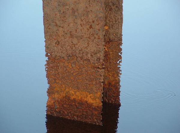 Steel beam sticking out vertically from the water showing major rust damage