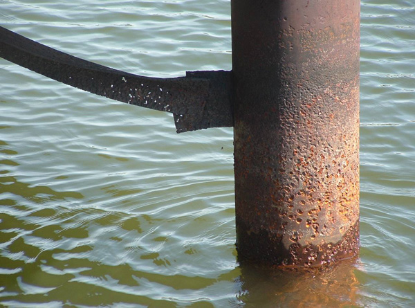 Piling with a crossbar attached to it, both showing major signs of rust failure.