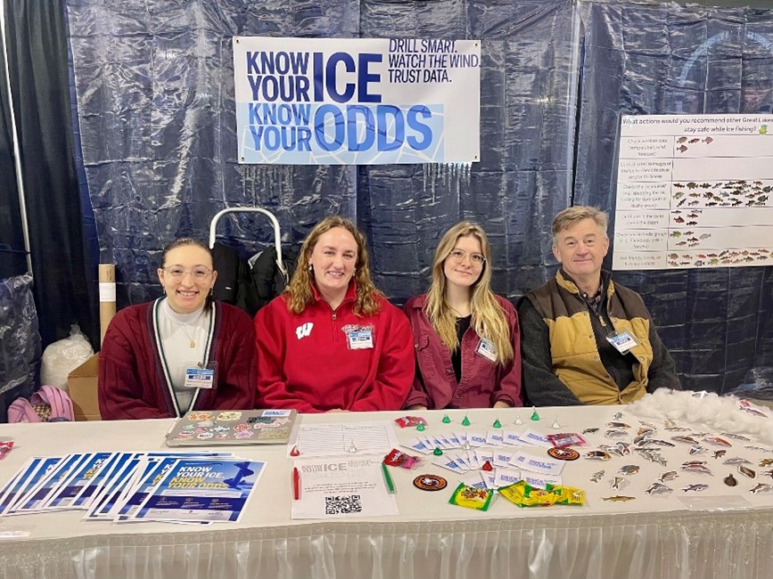 Researcher Bret Shaw and three student researchers sit at a table at the Ice Fishing Expo ready to talk to people about ice safety.