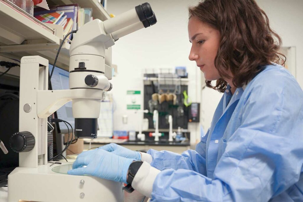 A woman moving something into the viewing platform of a microscope.